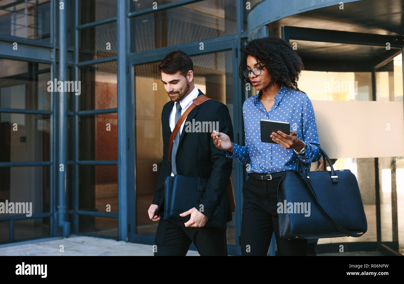 Two business colleagues walking out of office building. Corporate business professionals walking together and talking. Stock Photo