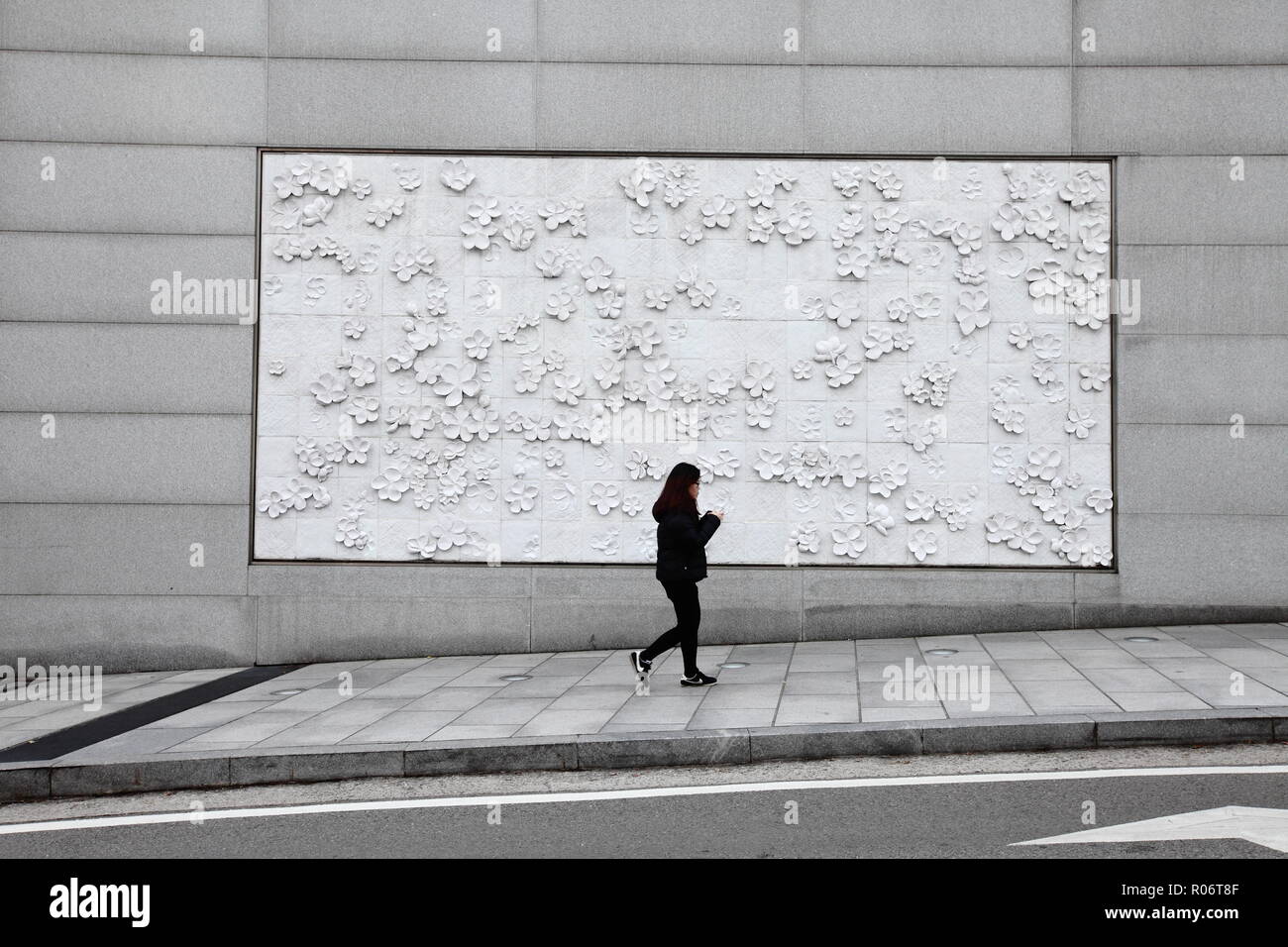 An outdoor flower wall art at Ewha womans university in Seoul, a lady dress in all black walk across the street, South Korea. Stock Photo