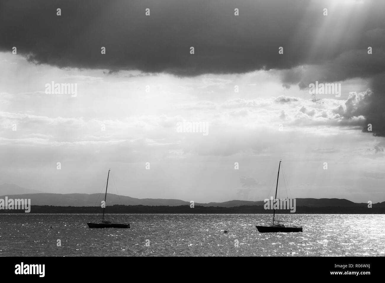 A couple of empty, little sailboat on a lake, beneath a moody sky with sun rays filtering through. Stock Photo