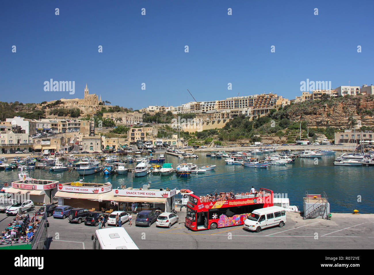Mgarr, Malta - May 2018: Gozo Ferry Terminal bay view of port with touristic bus, cars, snack bars, yachts and church on background Stock Photo