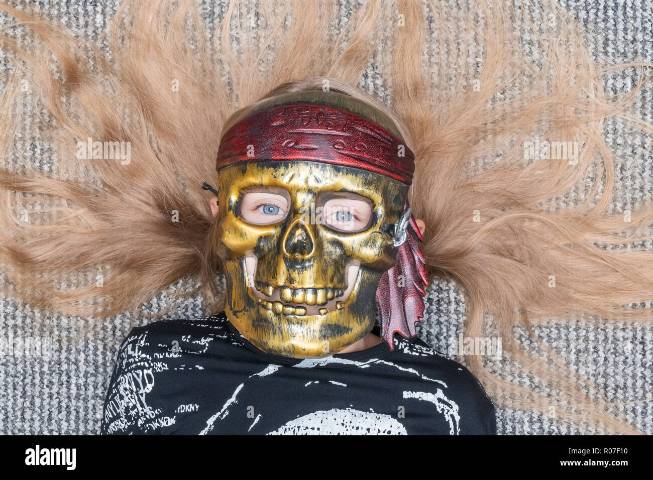 child in a skull mask lying on the floor with disheveled hair Stock Photo