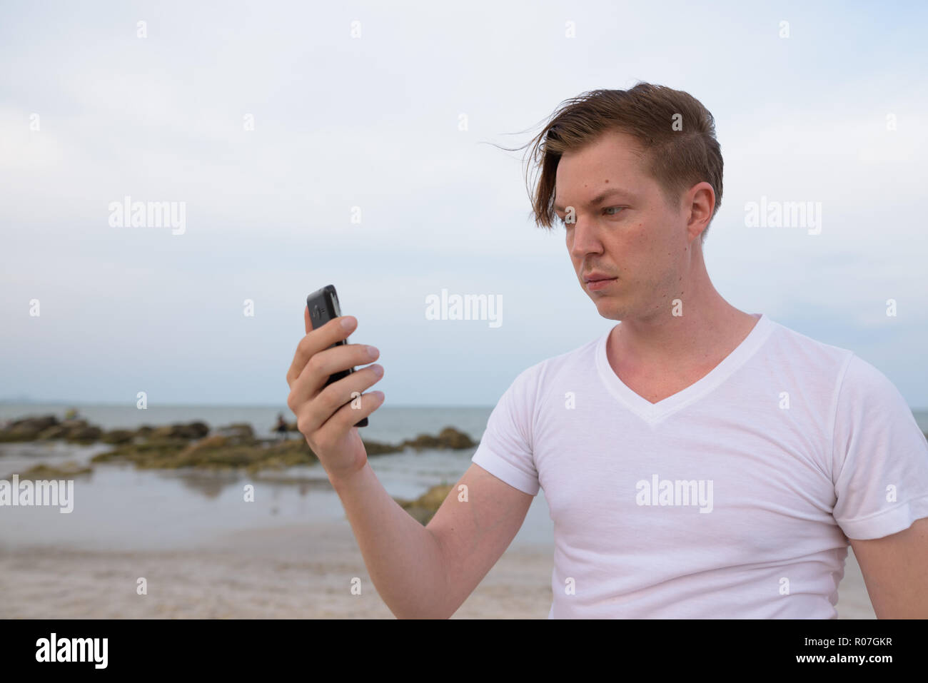 Young handsome man using mobile phone at the public beach of Hua Stock Photo
