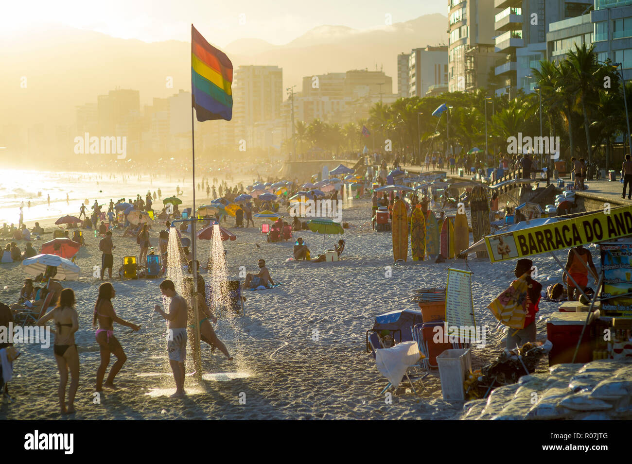 RIO DE JANEIRO - CIRCA FEBRUARY, 2018: Young people shower under a gay pride rainbow flag as the sun sets above Ipanema Beach, Stock Photo