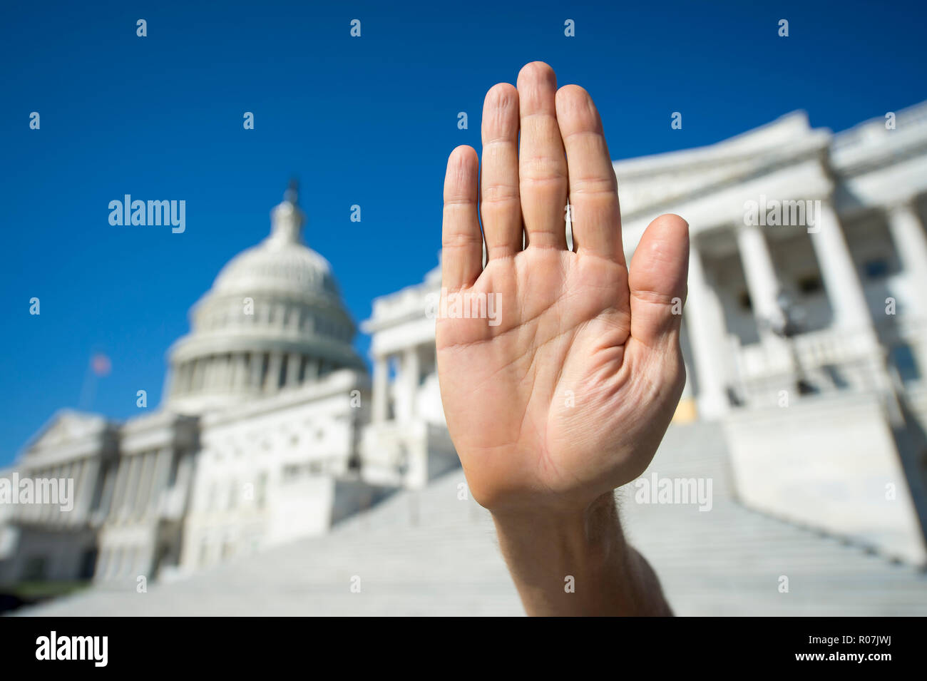 Hand held up in full stop gesture with palm out in bright sun in front of the Capitol Building in Washington DC, USA Stock Photo