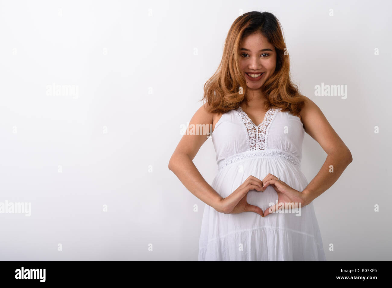 Studio shot of young happy Asian pregnant woman smiling and maki Stock Photo