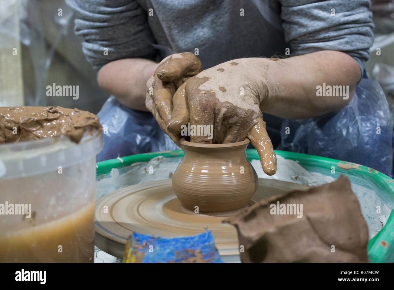 male hands of a student in pottery training courses, reportage photography. making a pot of red clay on a potter's wheel Stock Photo