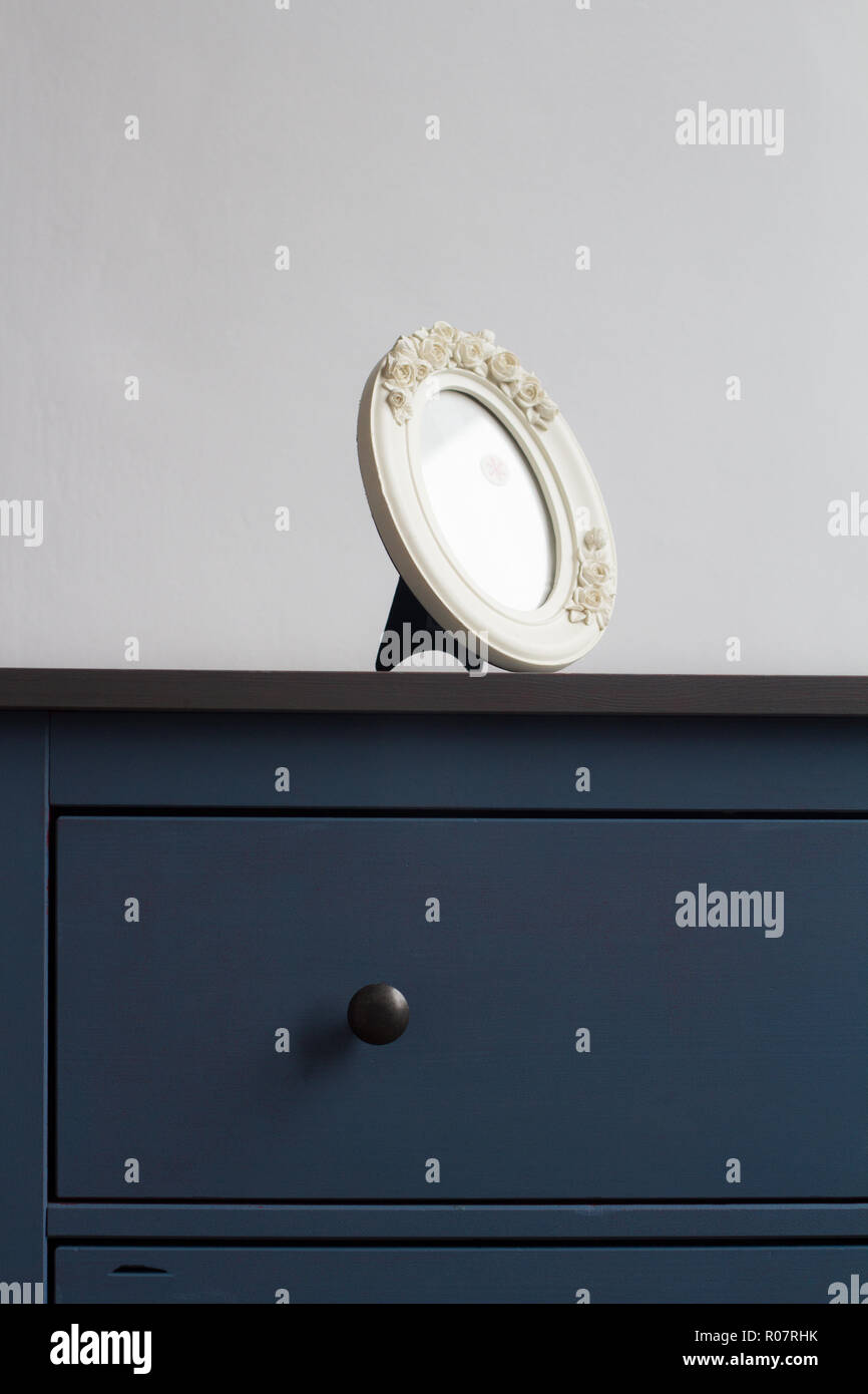 vertical front view detail of white round picture frame on blue vintage wooden chest of drawers with black handles against wall in natural light copys Stock Photo