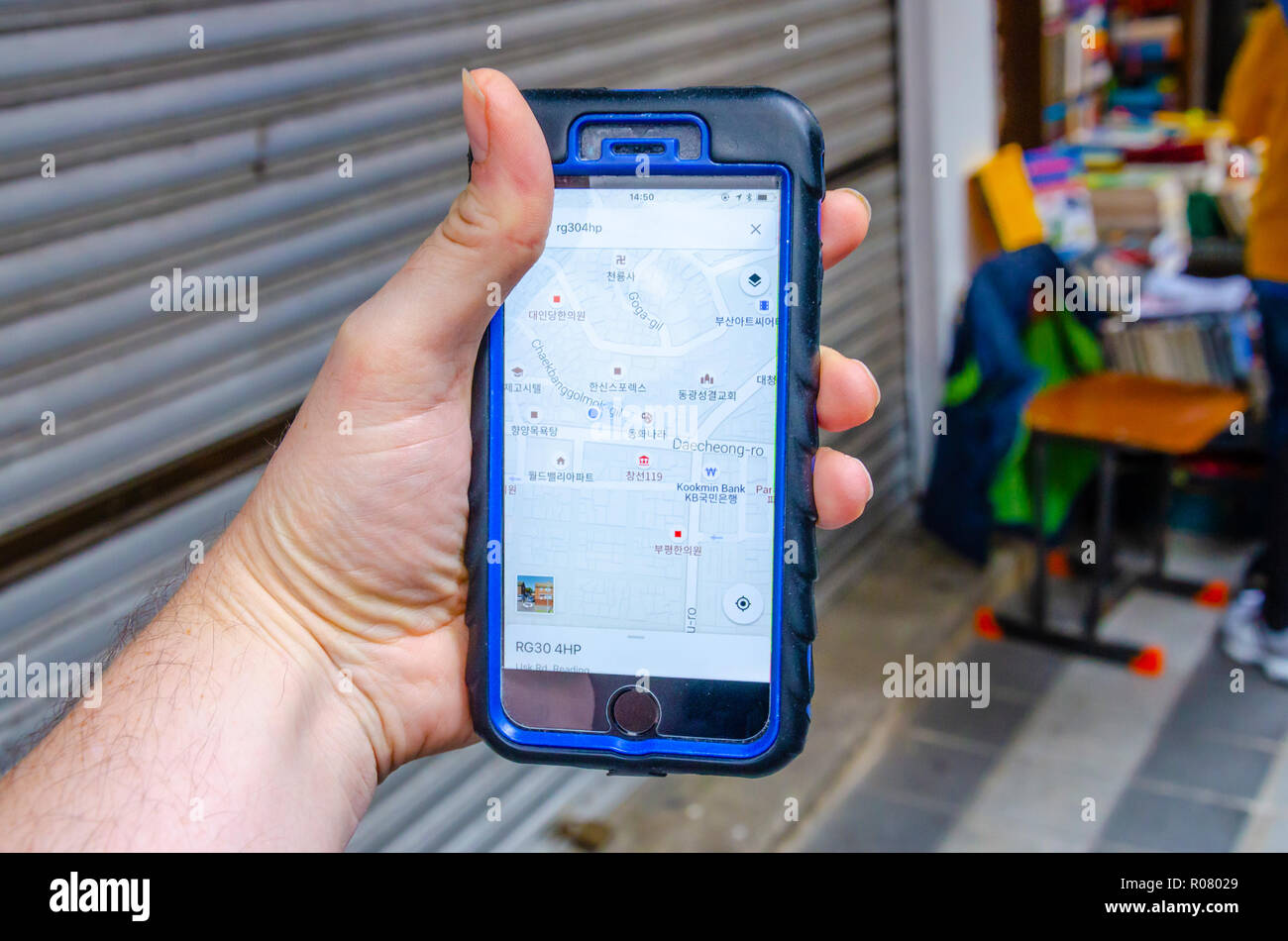 A male hand holds an iphone mobile phone and is using the Google Maps application to navigate around the city of Busan in South Korea. Stock Photo