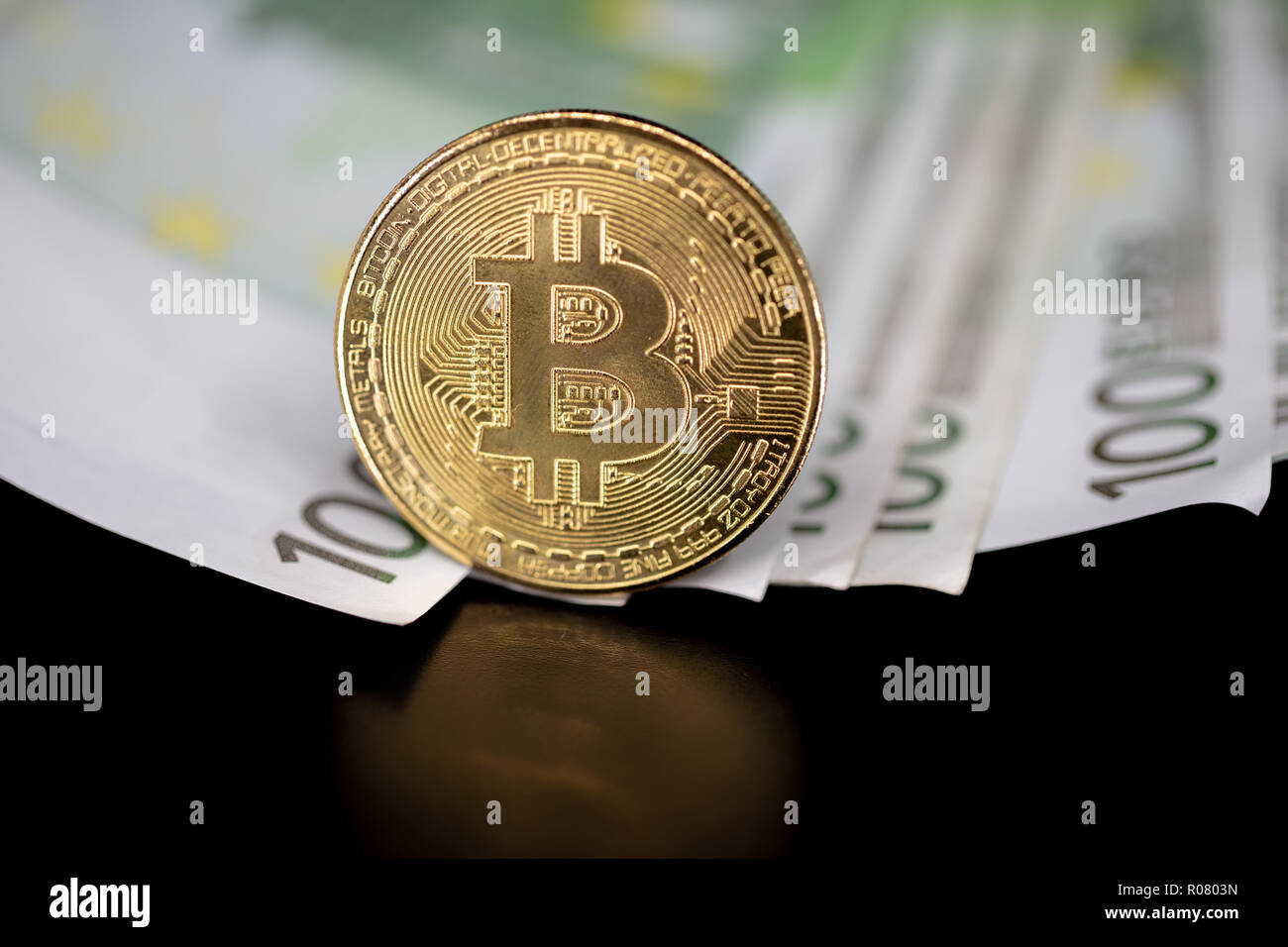 Bitcoin token on black with reflection, with a big pile of euro banknote money in the background Stock Photo