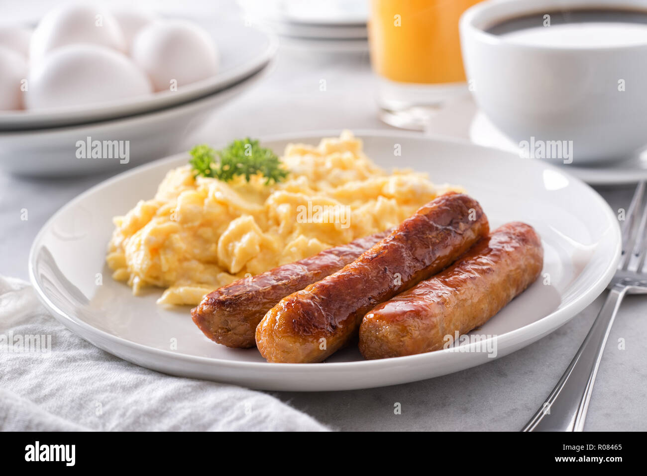 A plate of delicious scrambled eggs and breakfast sausage with coffee and orange juice. Stock Photo