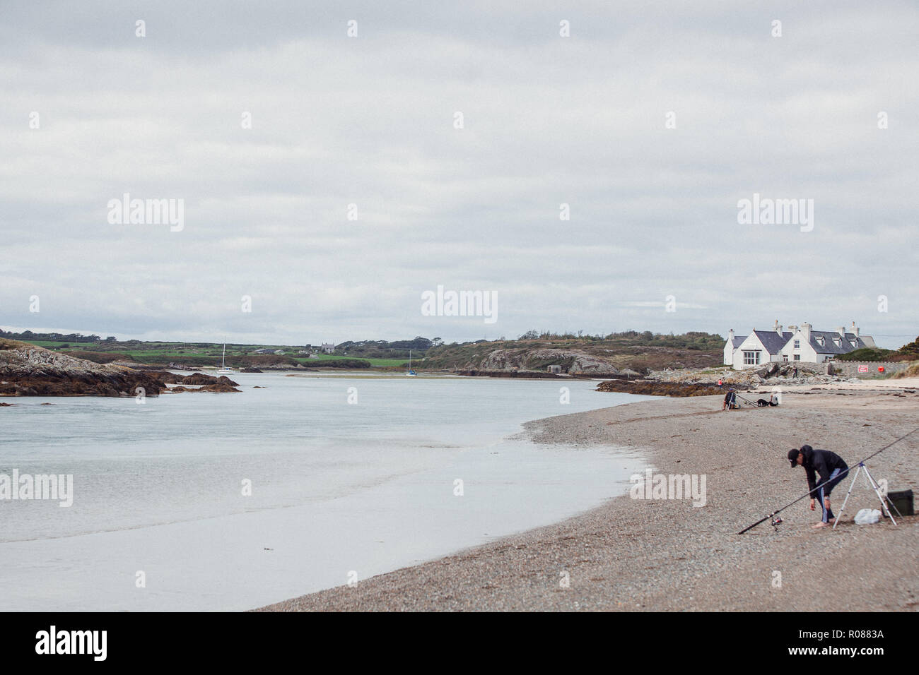 Man fishing from the beach in the Irish Sea on the coast of Anglesey, North Wales, near Rhosneigr, by the Inland Sea, UK Stock Photo