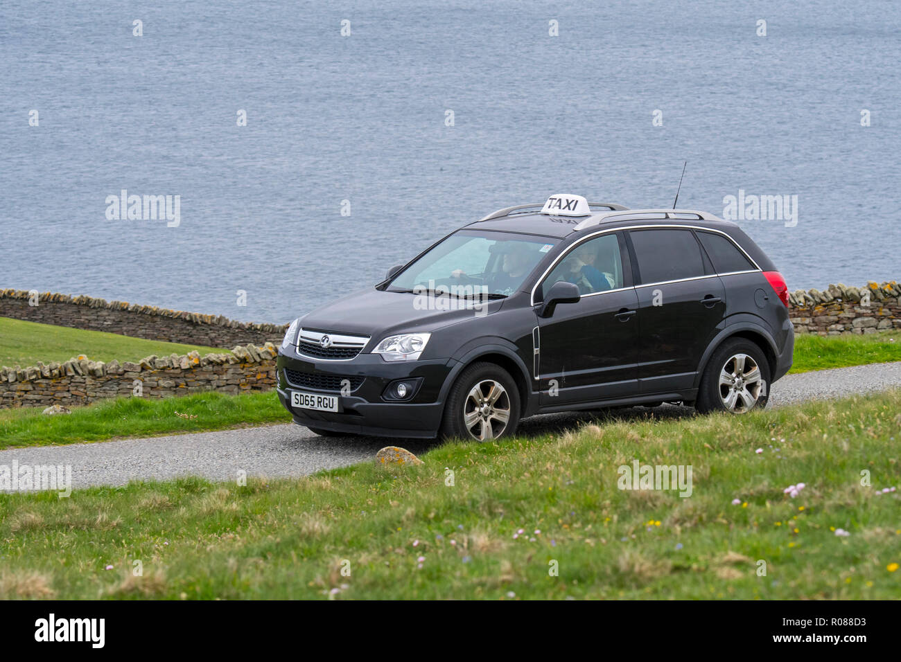 Taxidriver driving taxi with customer along desolate coastal road in Scotland, UK Stock Photo