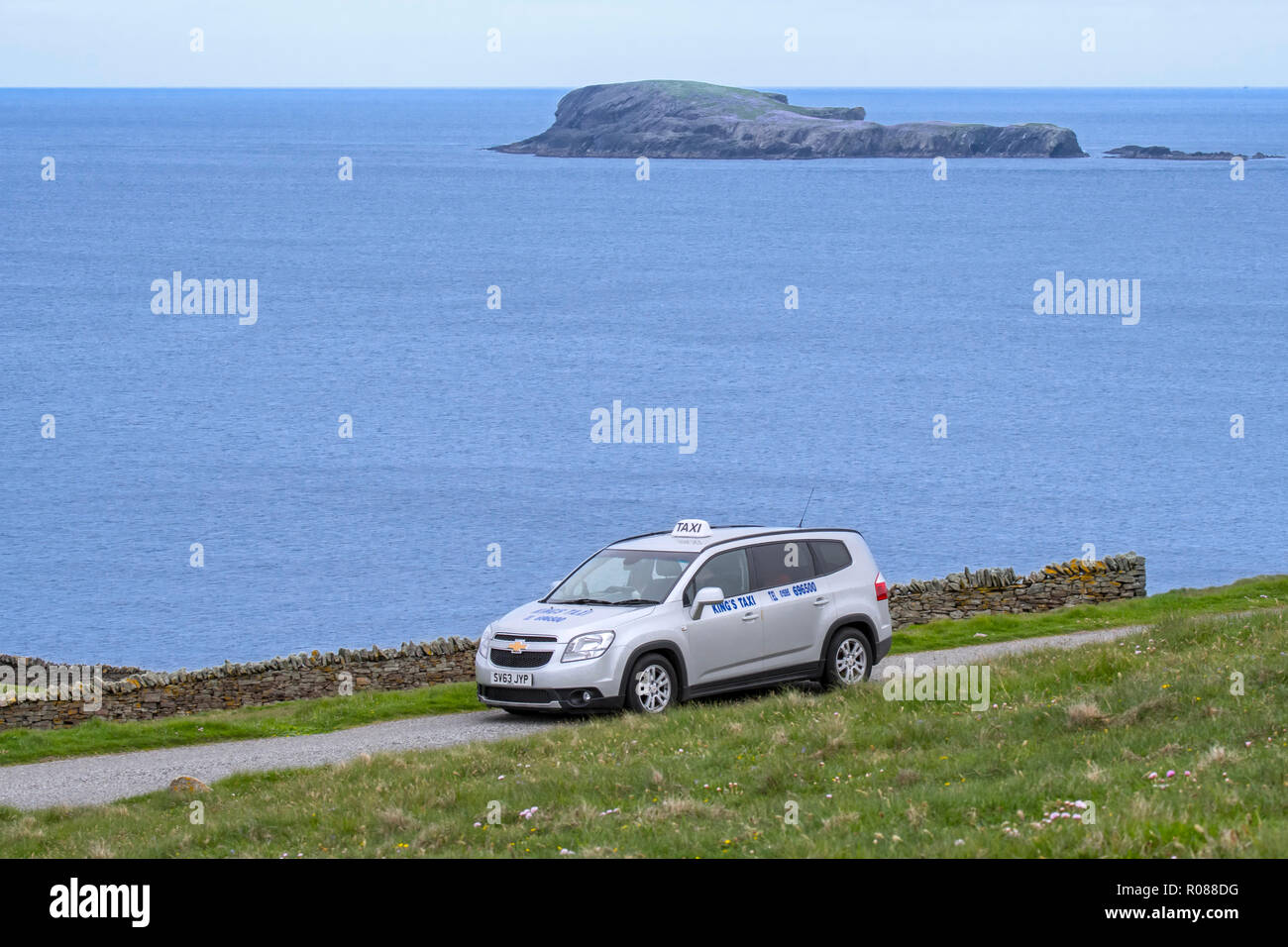 Taxidriver driving King's taxi with tourists along desolate coastal road in Shetland, Scotland, UK Stock Photo