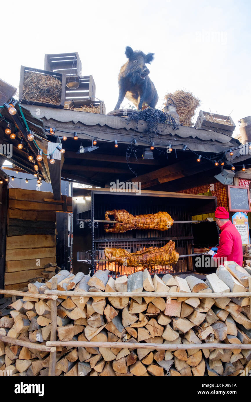 Man in red hat & jacket roasts a hog on a spit over open fire at Bavarian Village, Winter Wonderland Christmas Festival, Hyde Park, London. Dec.2016 Stock Photo