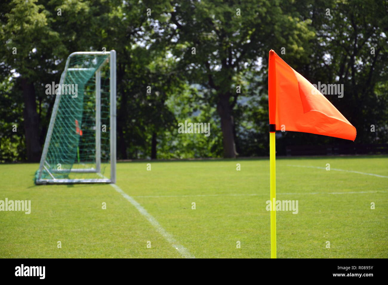 Orange vivid corner flag on fresh green football ground, trees in background, sunny summer day Stock Photo