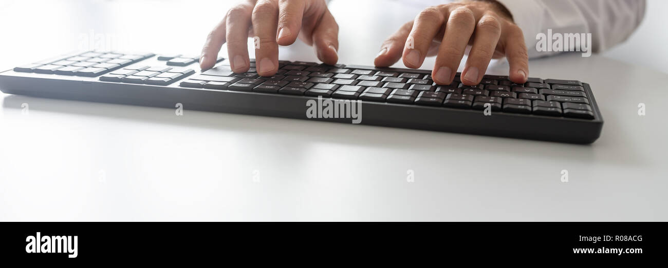 Wide view image of programmer using computer keyboard on white office desk. Stock Photo