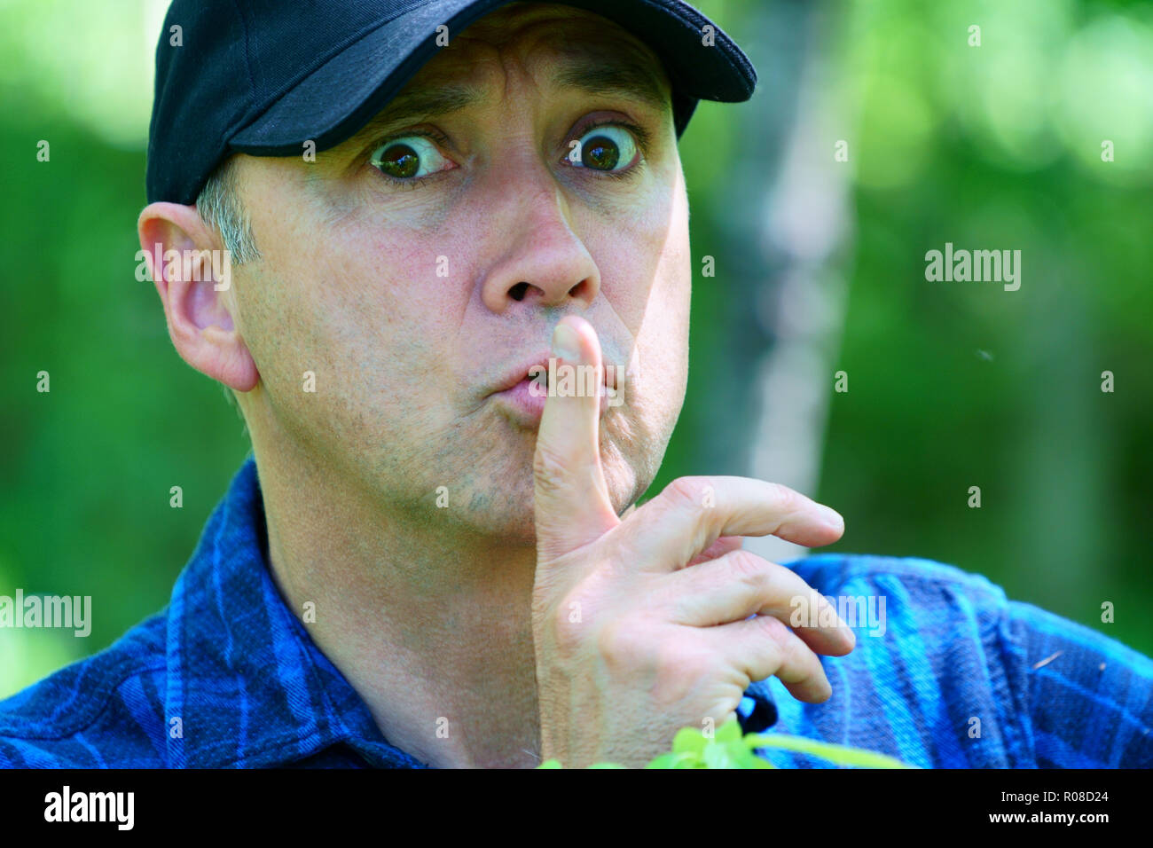 A caucasian curious man is looking away while hiking in the forest wearing a blue check shirt and a black hat. Stock Photo