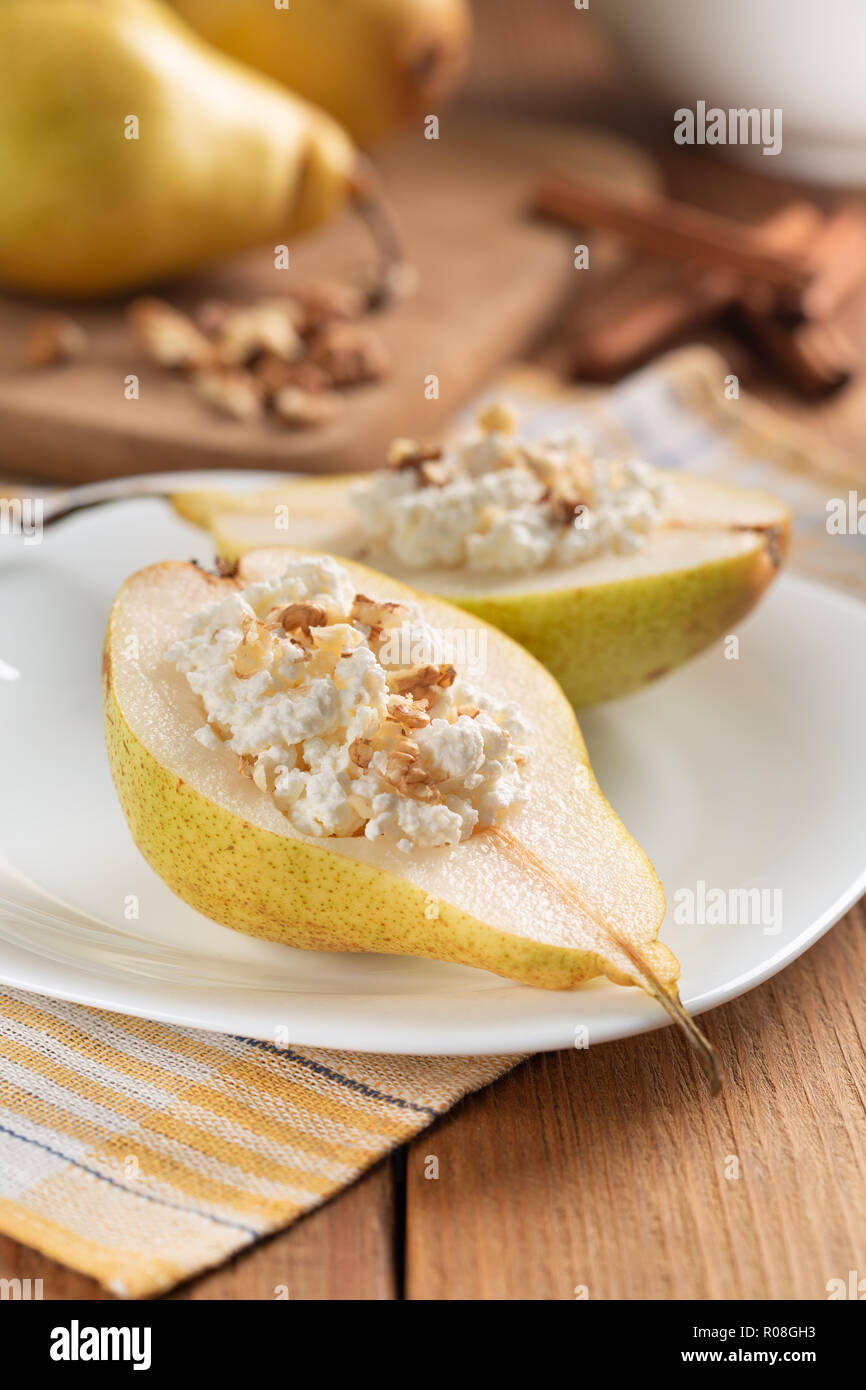 Half pears with cottage cheese and nuts on white dish. Wooden table, background blurred. Concept - Healthy food, healthy breakfast. Close-up. Stock Photo