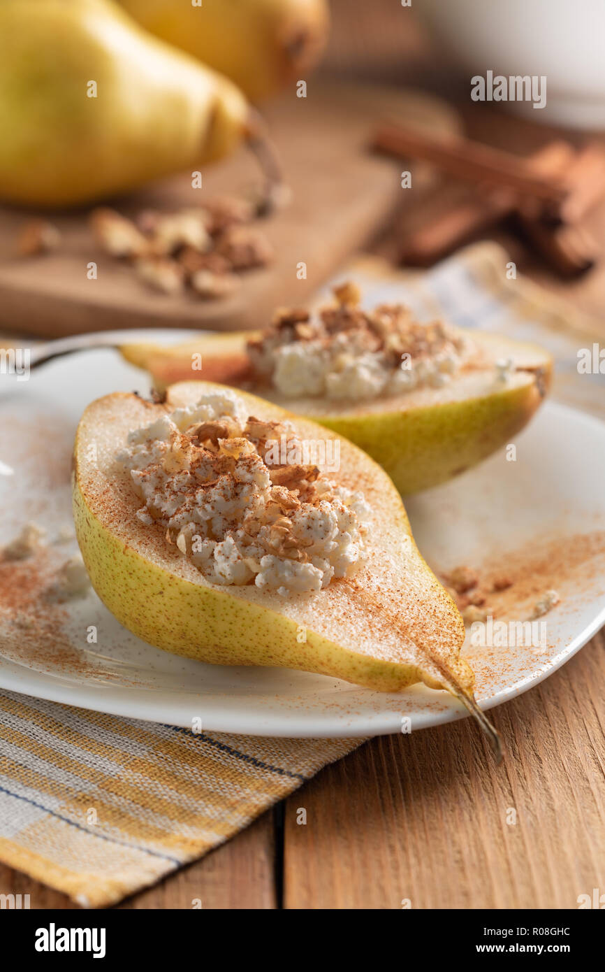 Half pears with cottage cheese, nuts and cinnamon on white dish. Wooden table, background blurred. Concept - Healthy food, healthy breakfast. Close-up Stock Photo
