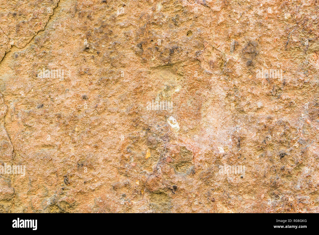 Horizontal photo with wall texture. Wall is covered by plaster which is worn and cracked. Several dark stones are placed on wall with send grains. Col Stock Photo