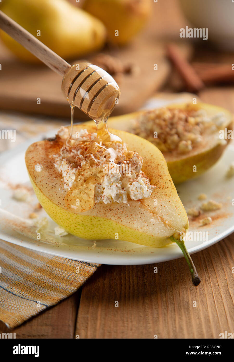 Half pear with cottage cheese, nuts, honey and cinnamon on white dish. It is watered with honey. Wooden table, background blurred. Concept - Healthy f Stock Photo