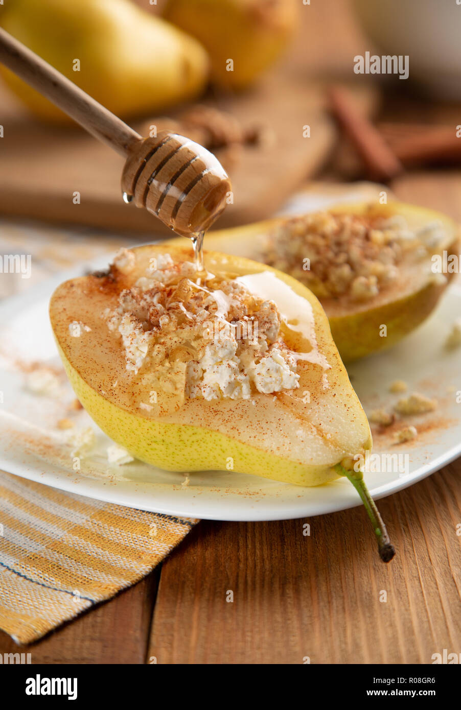 Half pear with cottage cheese, nuts, honey and cinnamon on white dish. It is watered with honey. Wooden table, background blurred. Concept - Healthy f Stock Photo