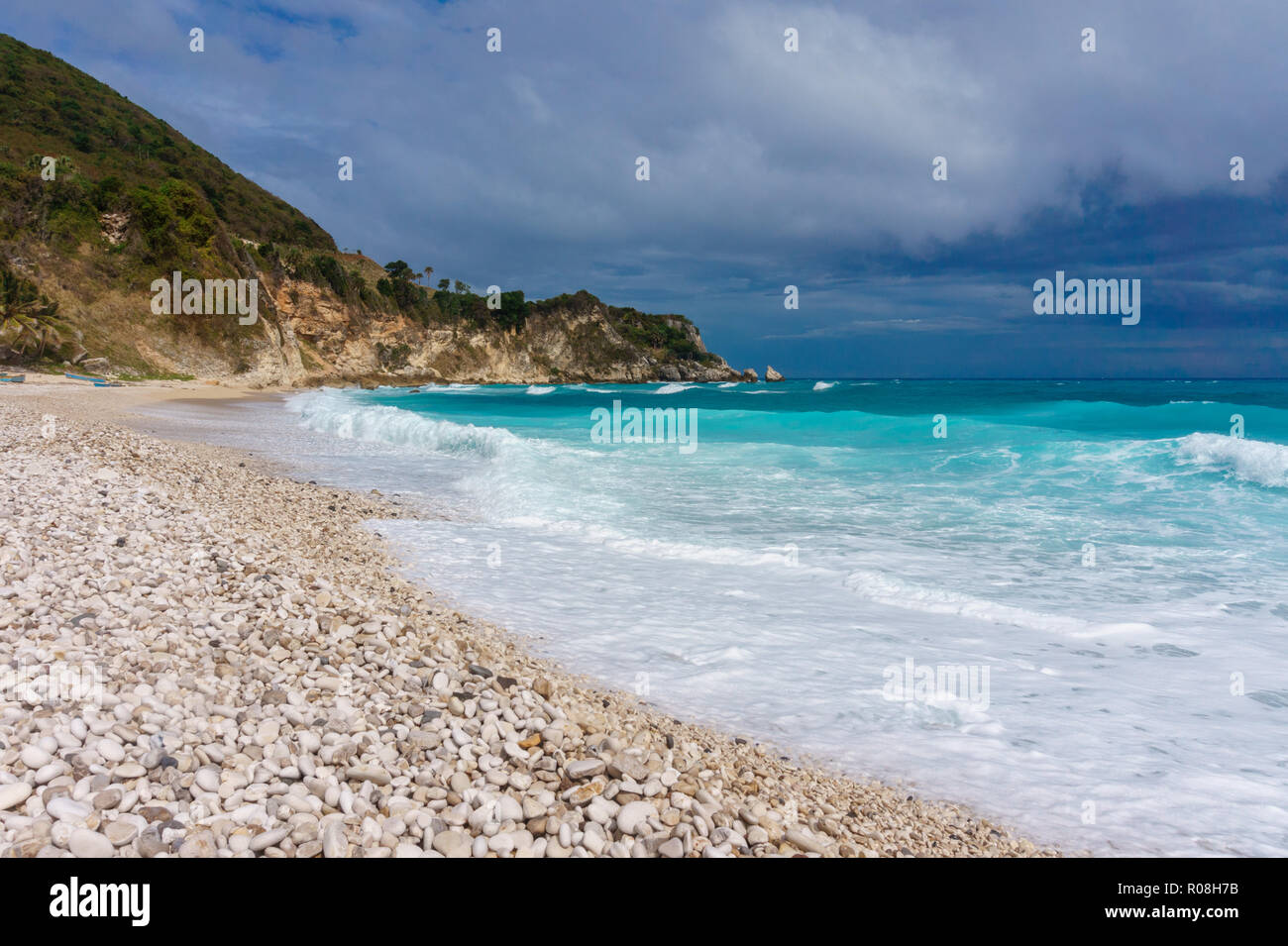 The storm in the Caribbean. Pebble beach, stormy blue sea, green hill and gray sky. Dominican Republic Stock Photo