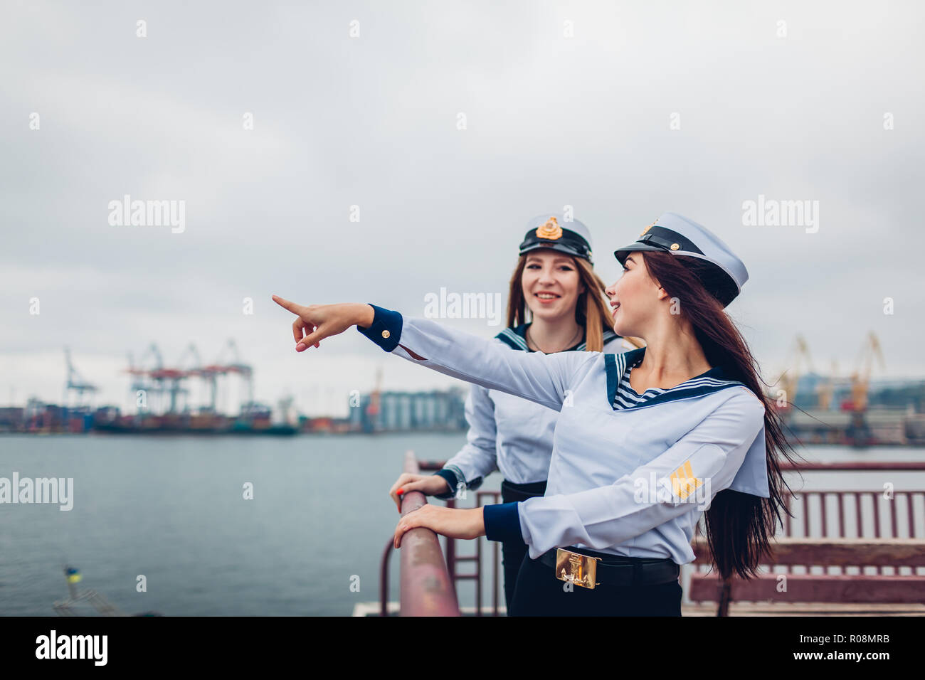 Two college women students of Marine academy walking by sea wearing uniform. Friends pointing into distance on pier. Navy fleet of Ukraine Stock Photo