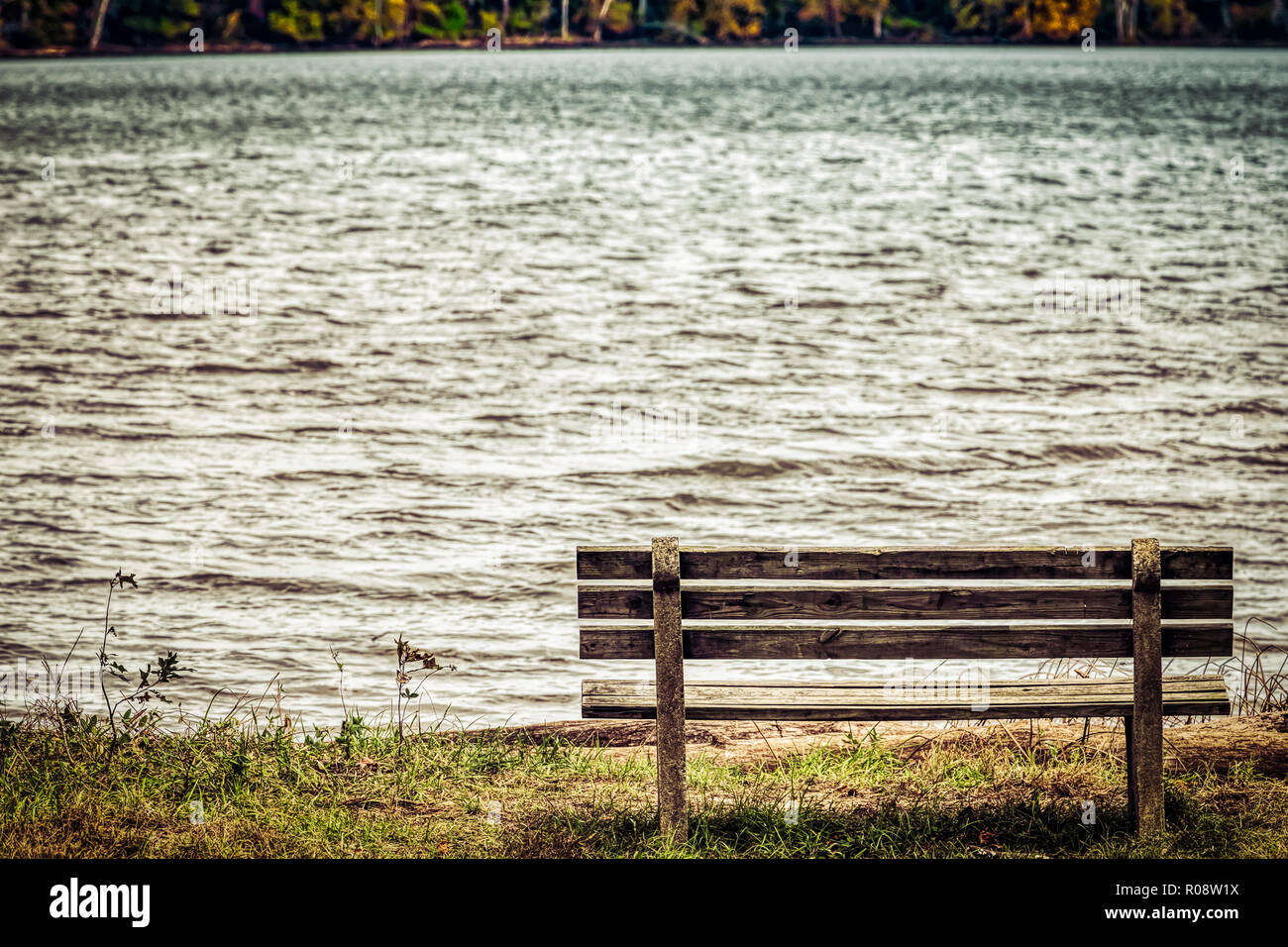 An empty park bench looks over a Virginia bay with fall colors appearing on the other side. Stock Photo