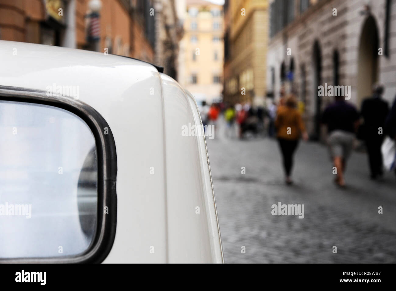 A parked Fiat 500 in the streets of Rome, some people on the background ...
