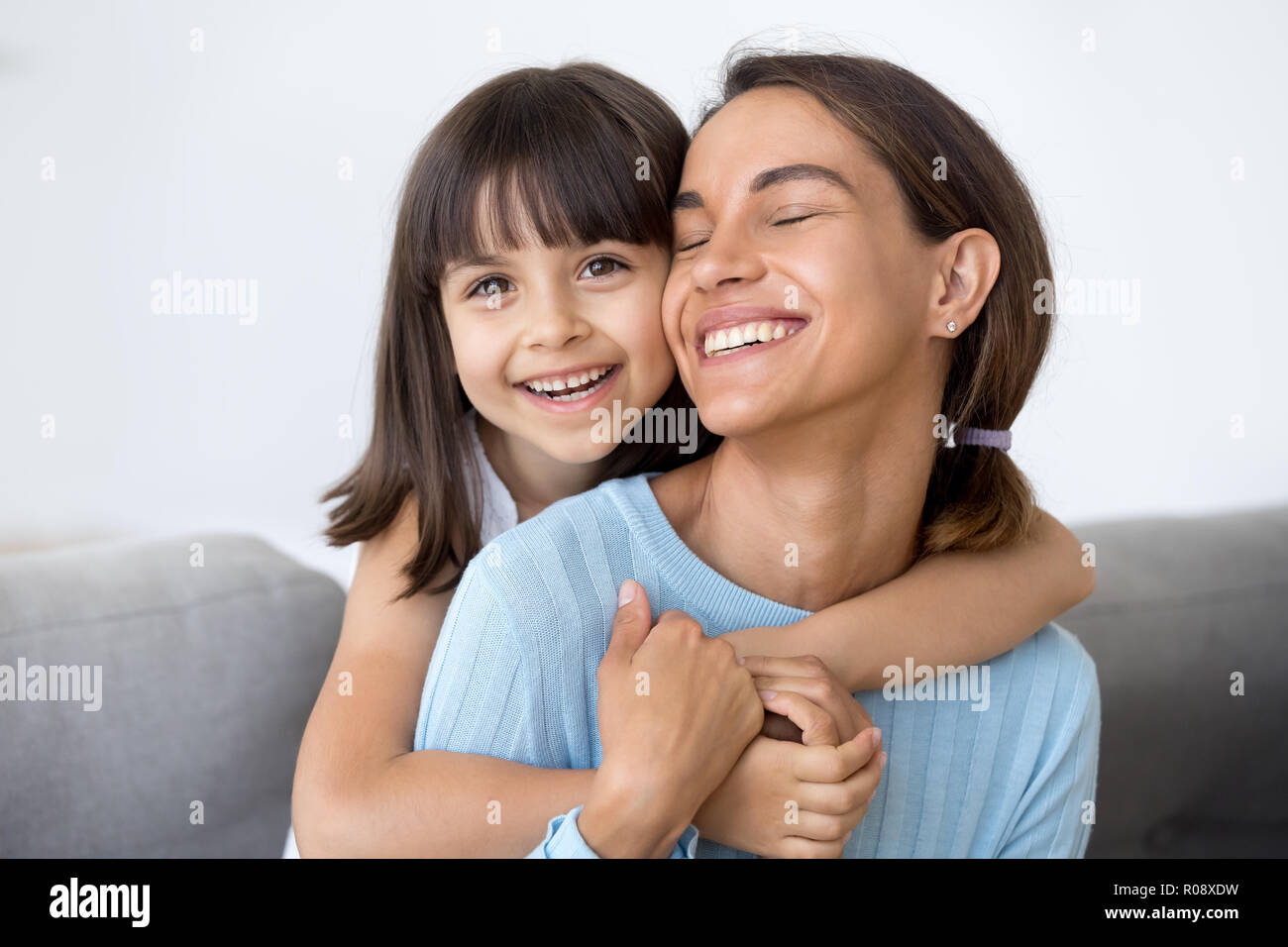 Laughing mother and daughter hugging sitting on sofa Stock Photo