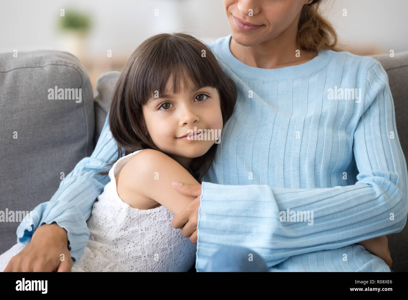 Daughter sitting embracing mother looking at camera Stock Photo