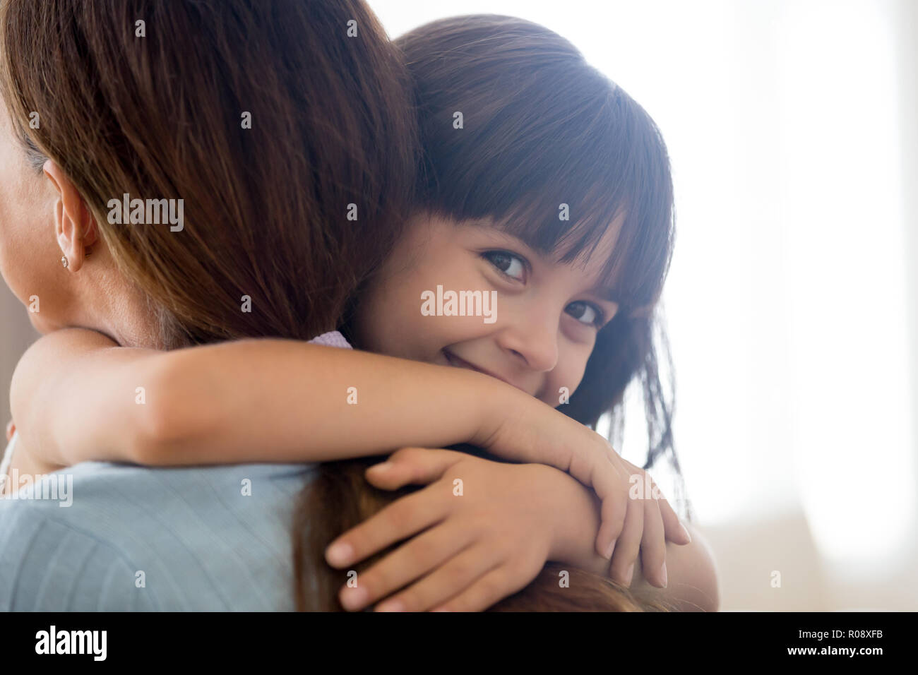 Happy daughter looking at camera embracing mother  Stock Photo