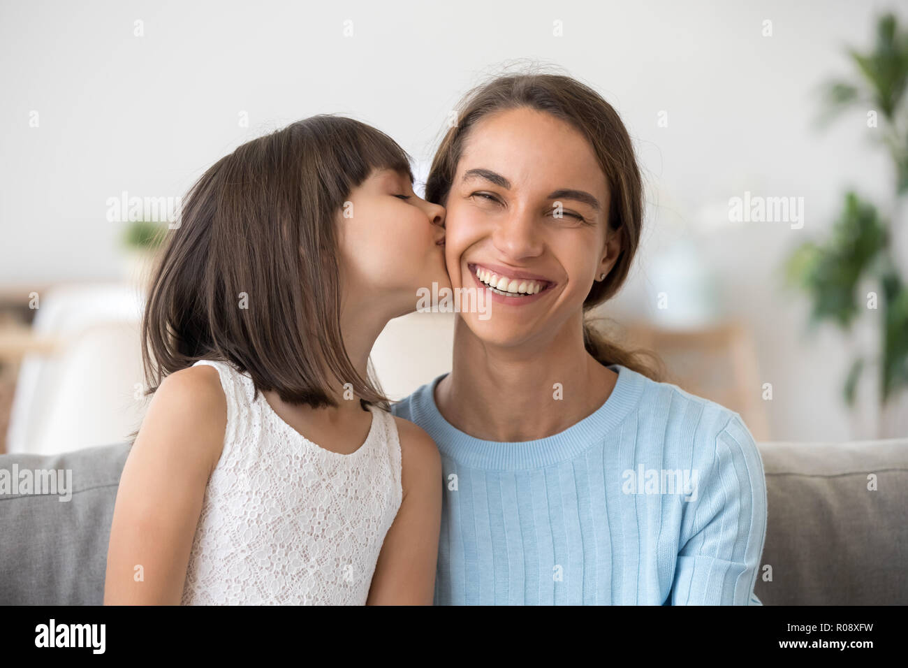 Daughter kissing mother on cheek have fun together at home Stock Photo