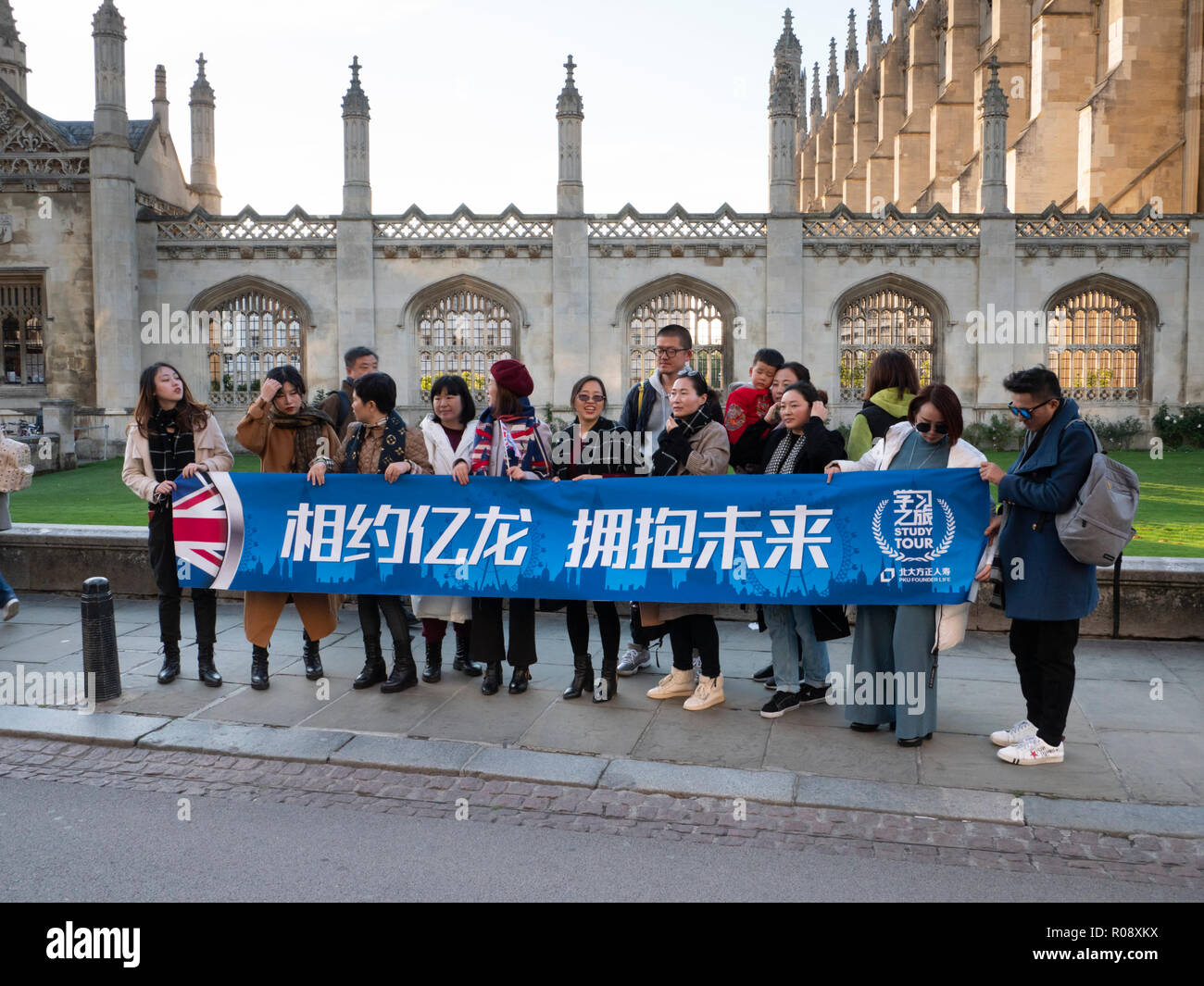 A large group of Chinese Tourists standing in King's Parade Cambridge UK holding a banner. Stock Photo