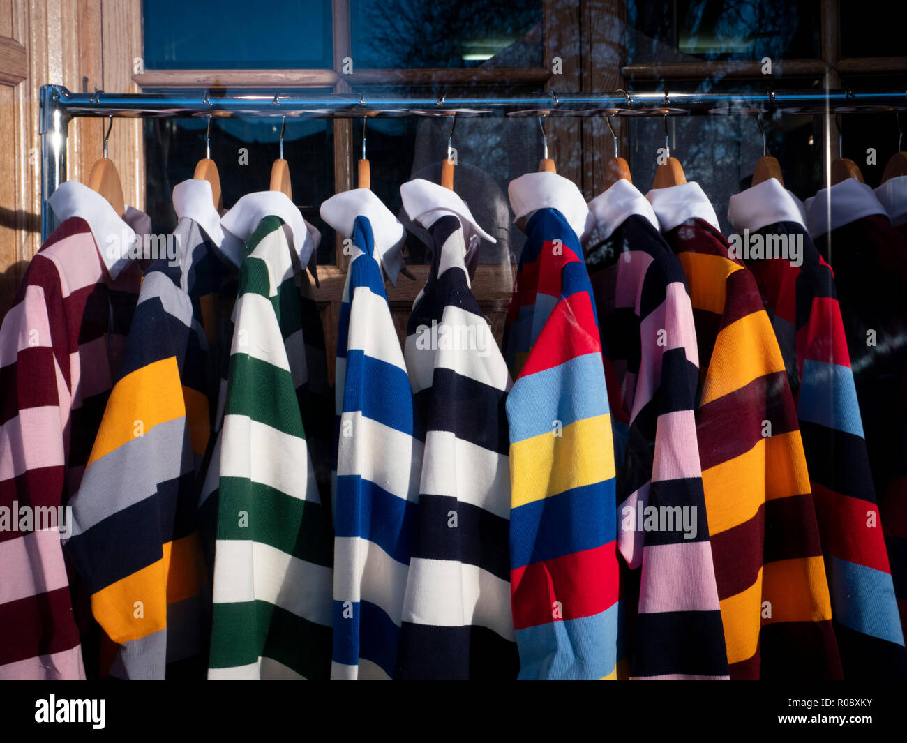 Colourful Cambridge University college rugby shirts hanging up for sale in a shop window display in Cambridge UK Stock Photo