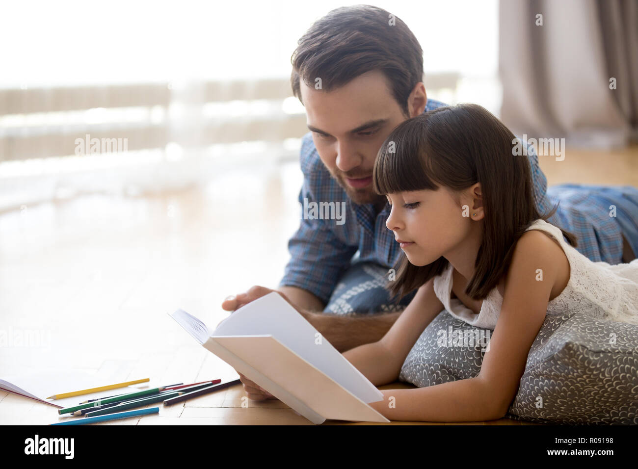Father and daughter lying on warm floor reading book Stock Photo