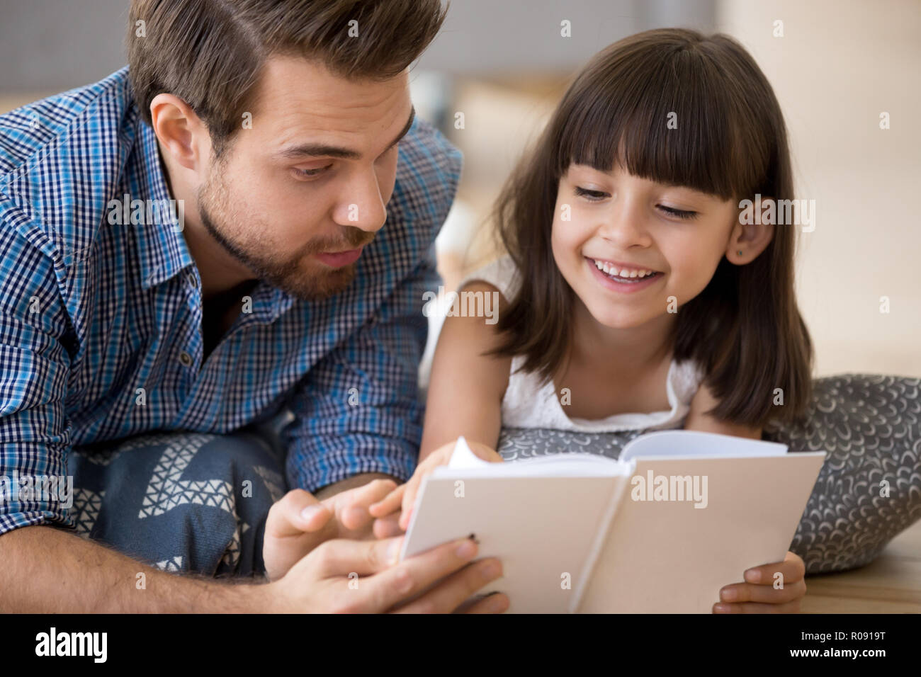 Father and child lying on warm floor reading a book Stock Photo