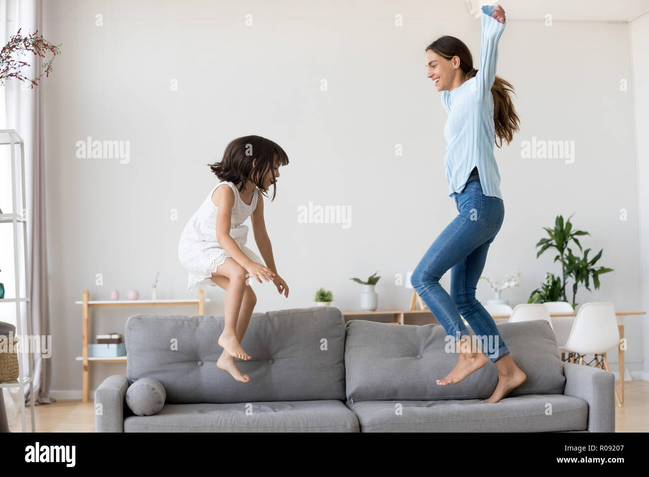 Mother and little daughter having fun jumping on couch Stock Photo