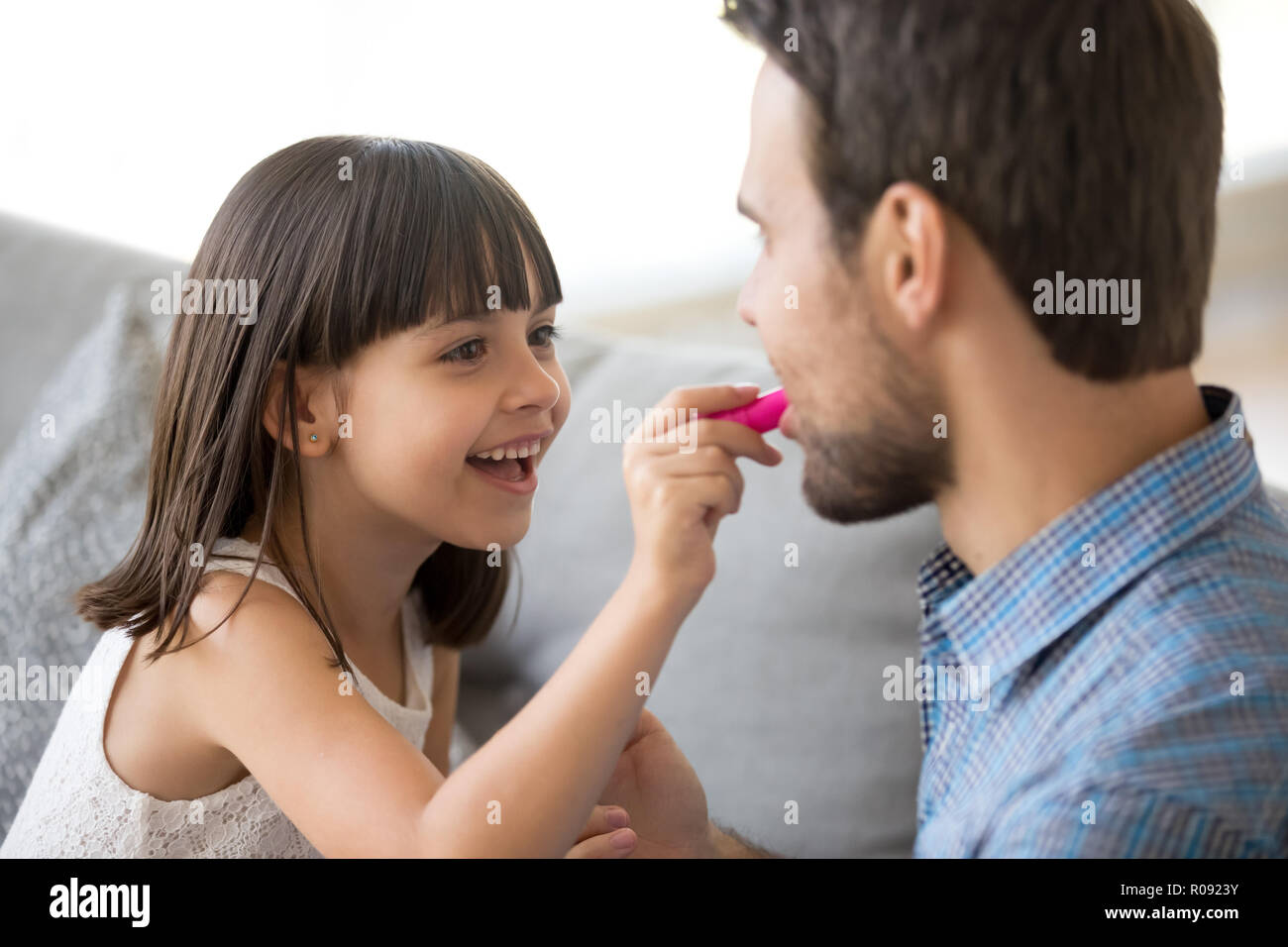 Funny daughter hold lipstick applying cosmetics on father lips Stock Photo