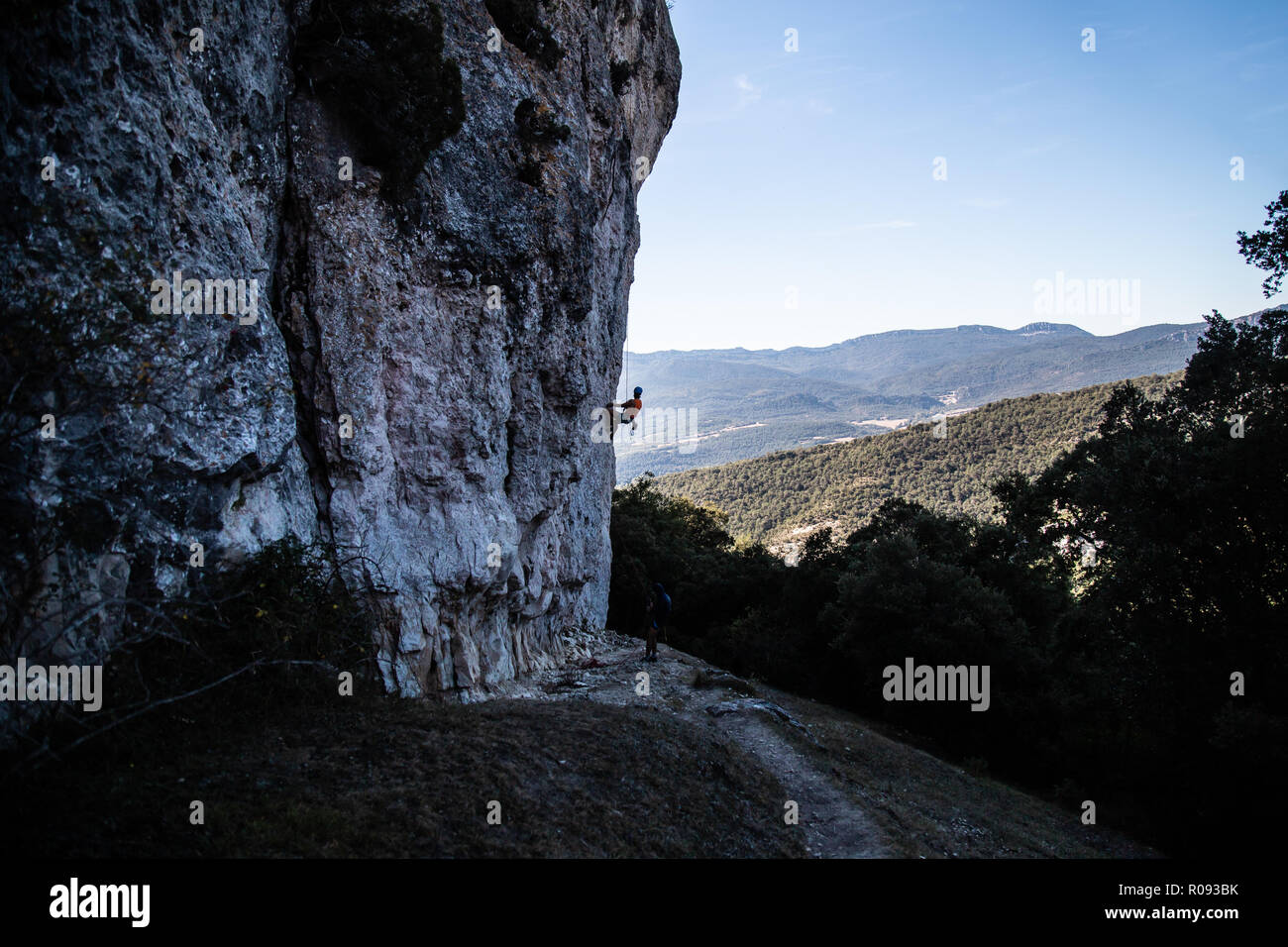 Young climber man climbing a large wall in a beautiful landscape in shadow Stock Photo