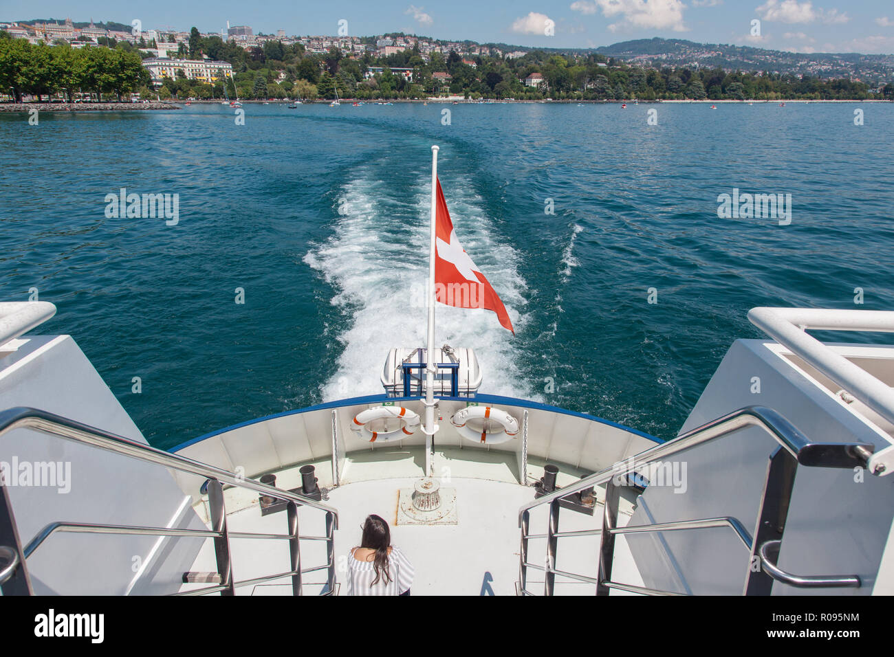 Young girl sitting on open deck at the back of passenger boat with Swiss flag leaving Lausanne port of Ouchy on Lake Leman (Geneva Lake), Switzerland Stock Photo