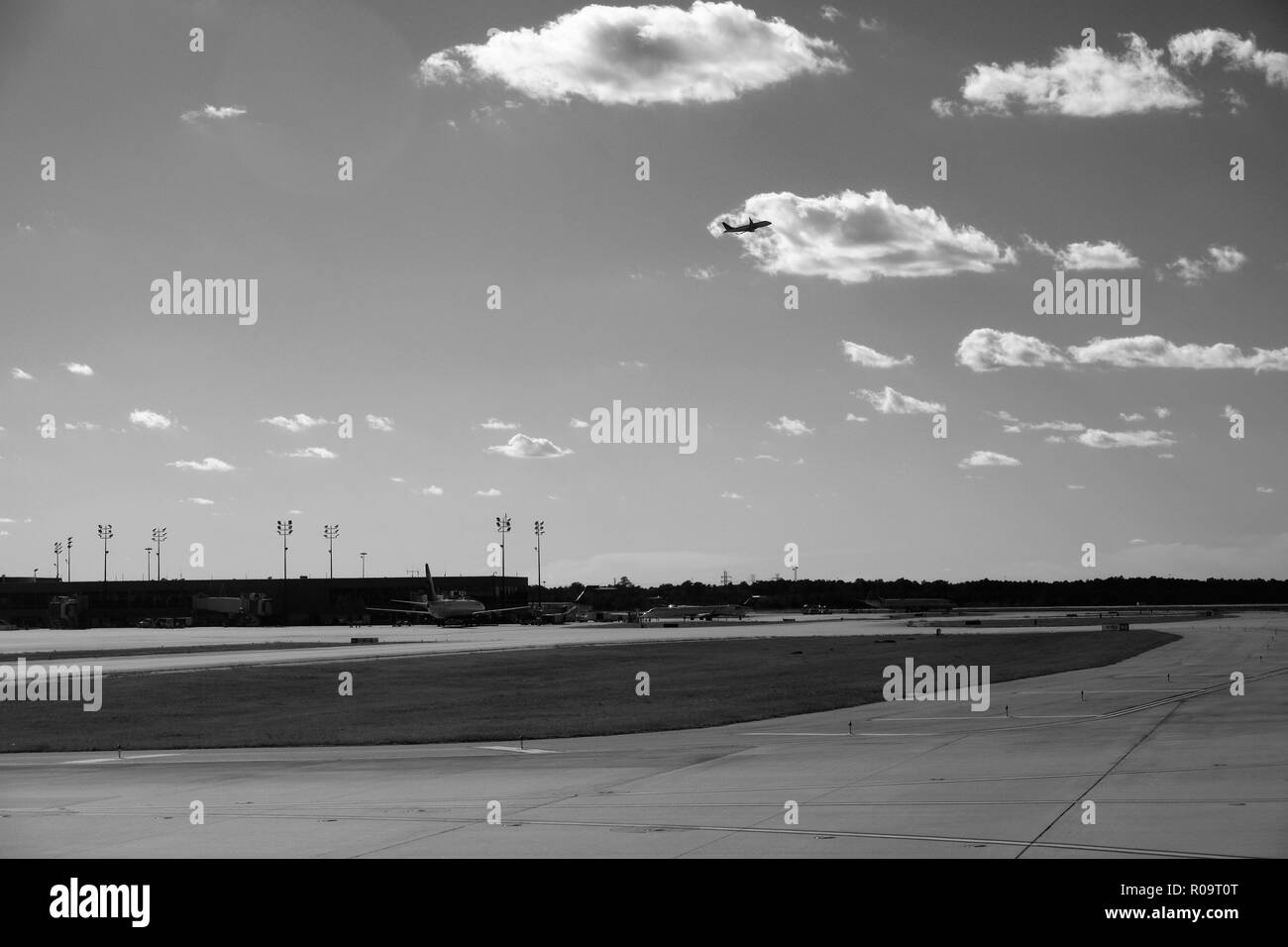 View of runway with airplanes at terminal and one on ascent in the open Texas sky; George Bush Intercontinental Airport, Houston, Texas, USA. Stock Photo