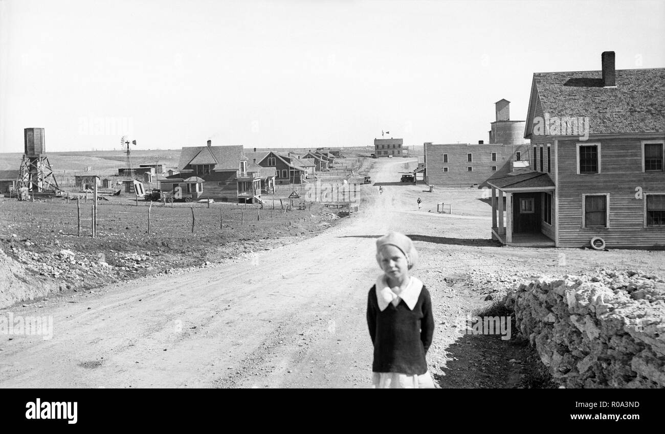 Portrait of Young Girl, Street Scene with Abandoned Grain Mill and Bank (both right) in Background, Mills, New Mexico, USA, Dorothea Lange, Farm Security Administration, May 1935 Stock Photo