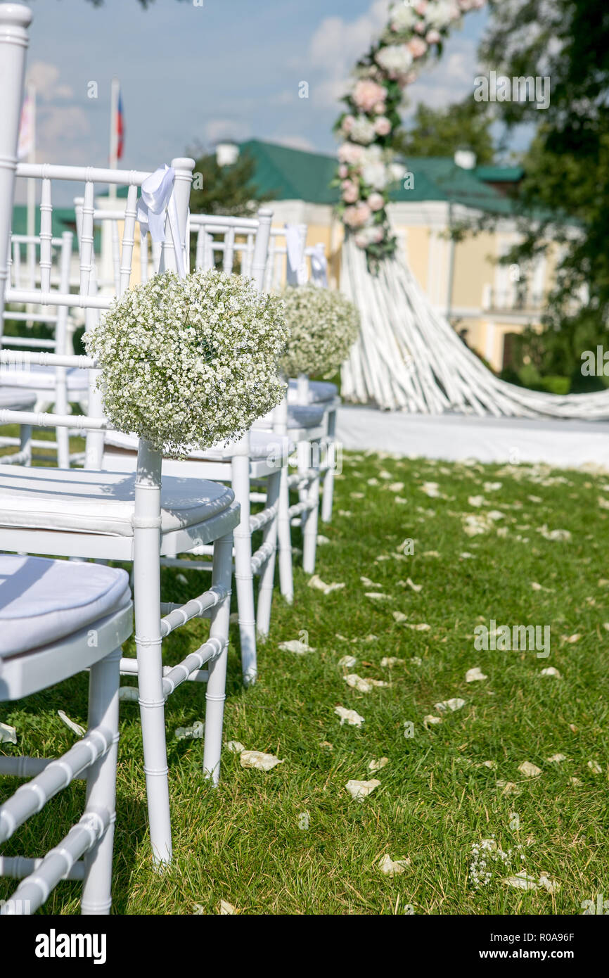 Summer outdoor wedding ceremony decoration. White chairs decorated with  gypsophila balls on the background of the arch for the wedding ceremony,  verti Stock Photo - Alamy