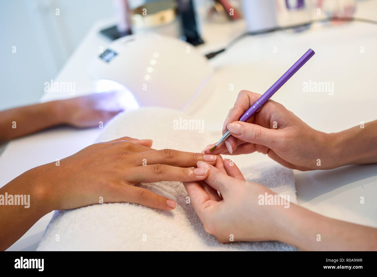 Close-up of beautician painting a woman's nails with a brush in a nail salon. Costumer receiving a manicure. Stock Photo