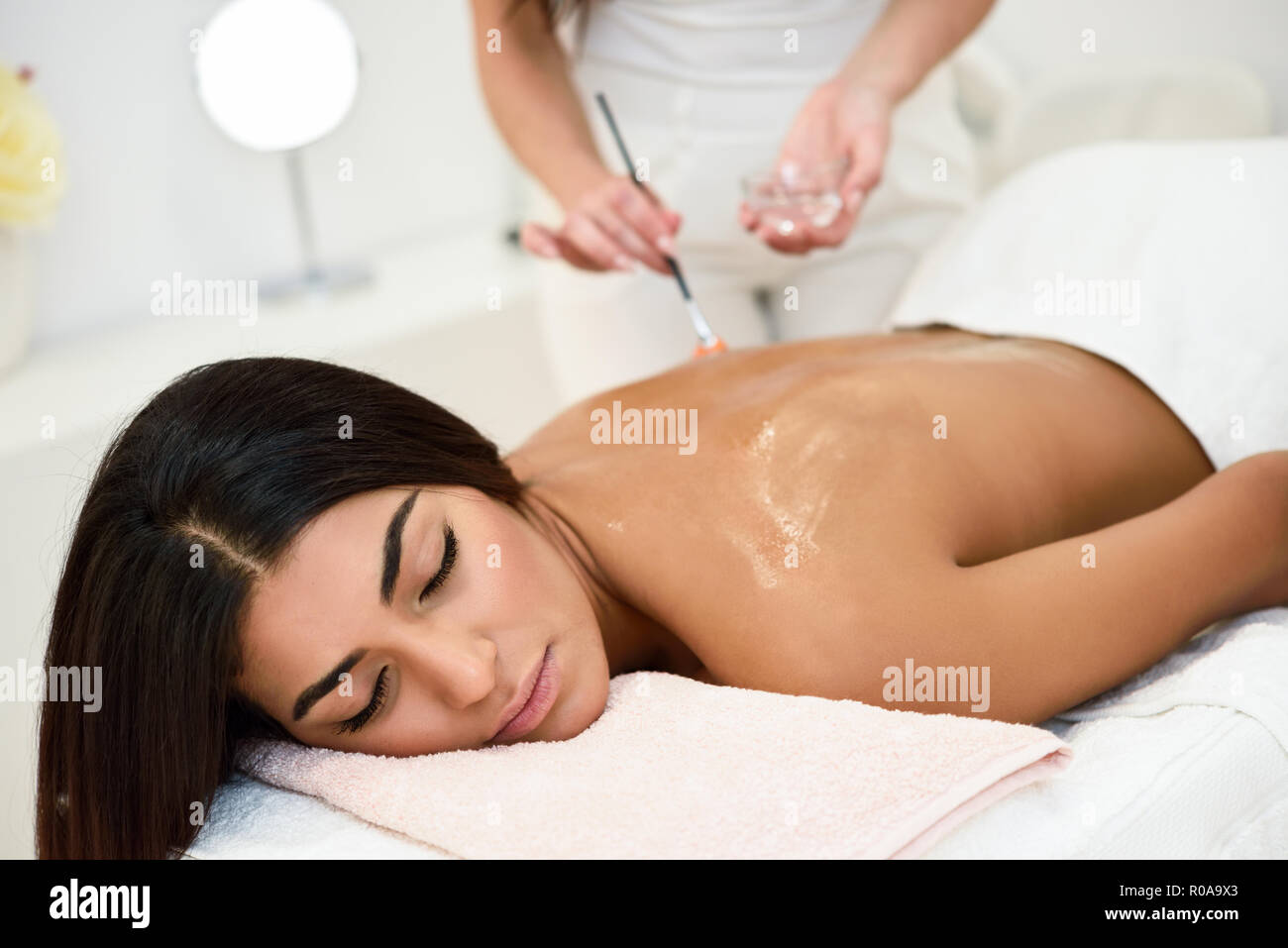 Arab woman receiving back massage treatment with oil brush in spa wellness center. Beauty and Aesthetic concepts. Stock Photo
