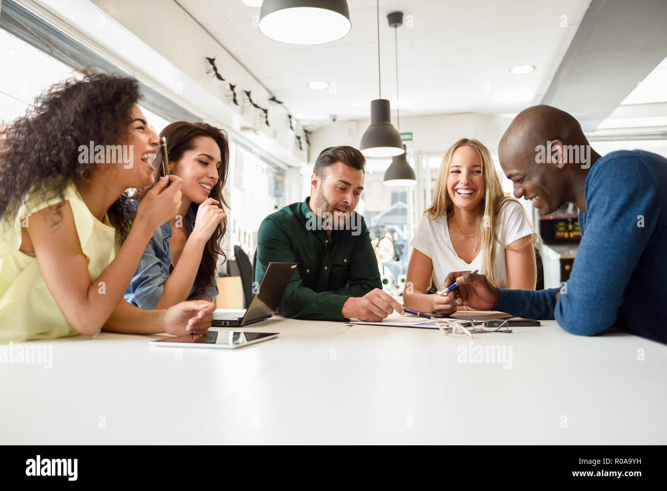 Five young people studying with laptop and tablet computers on white desk. Beautiful girls and guys working toghether wearing casual clothes. Multi-et Stock Photo