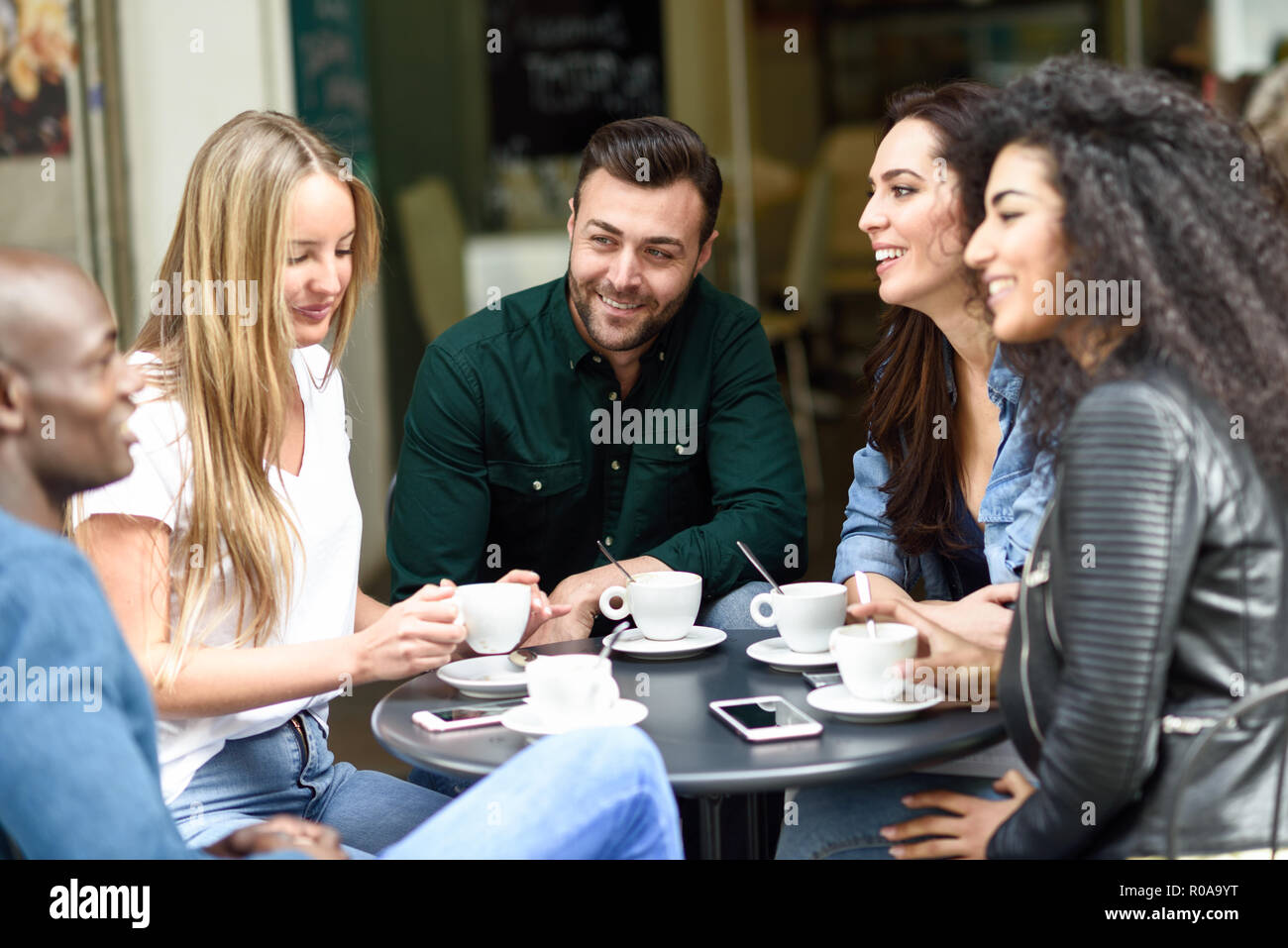 Multiracial group of five friends having a coffee together. Three women and two men at cafe, talking, laughing and enjoying their time. Lifestyle and  Stock Photo
