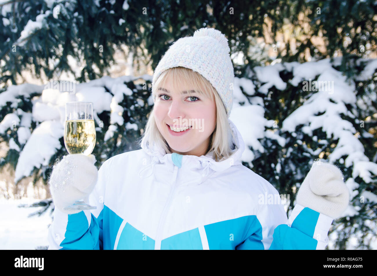 beautiful blonde girl with a glass of champagne sings and dances outdoors on a background of snowy fir-trees in winter Stock Photo
